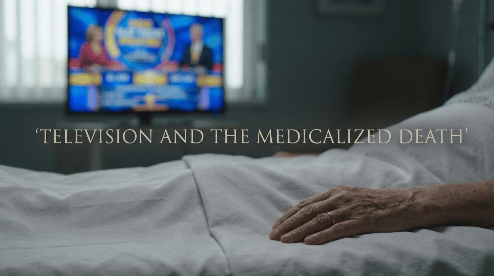 Elderly hand on hospital bed with glowing television in blurred background symbolizing medicalized death